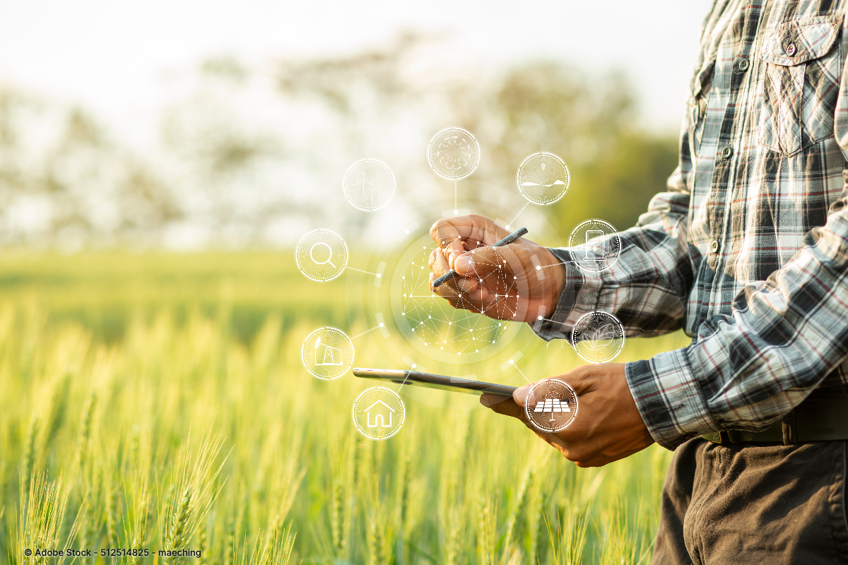 Ein Landwirt nutzt ein Tablet mit digitalen Symbolen im Getreidefeld und veranschaulicht den Einsatz moderner Landmaschinen Technologie heute.
